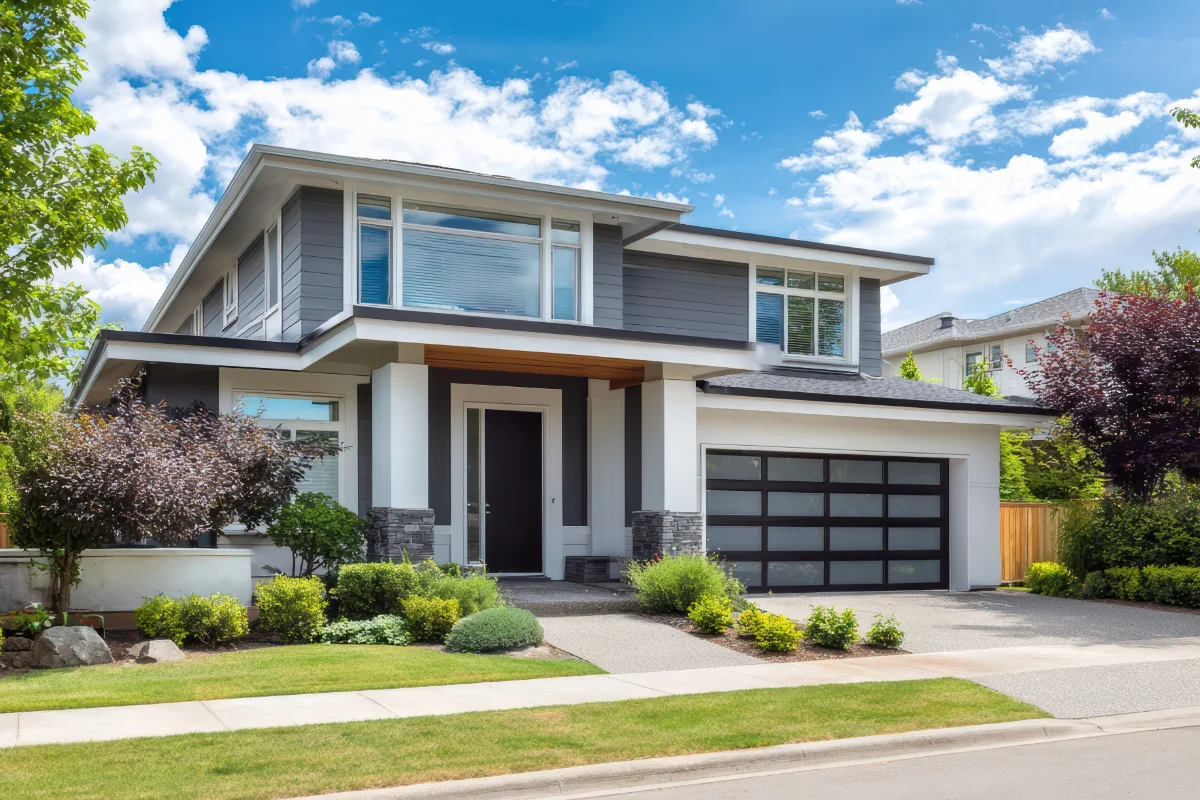 owners-representation-img-2 Two-story modern house with gray siding, black front door, and a two-car garage with frosted glass panels on a sunny street.